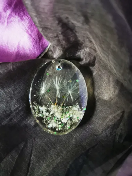Oval pendant with dandelion plant parts